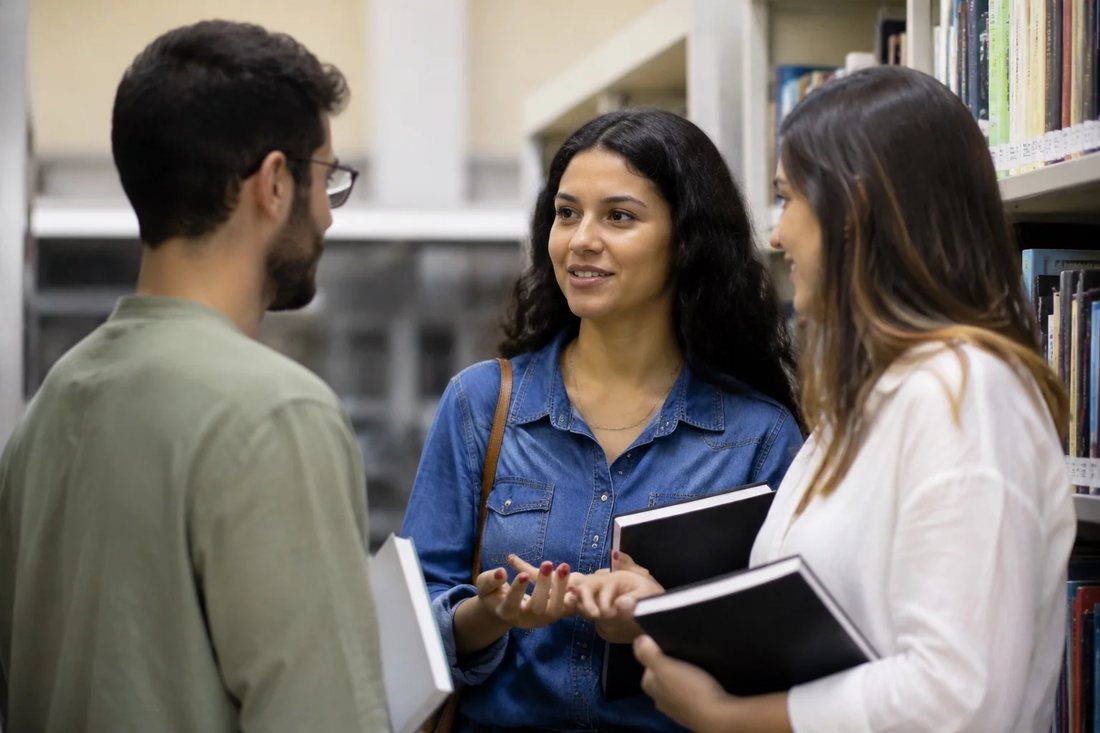 Alunos conversando em pé no corredor entre as prateleiras de uma biblioteca